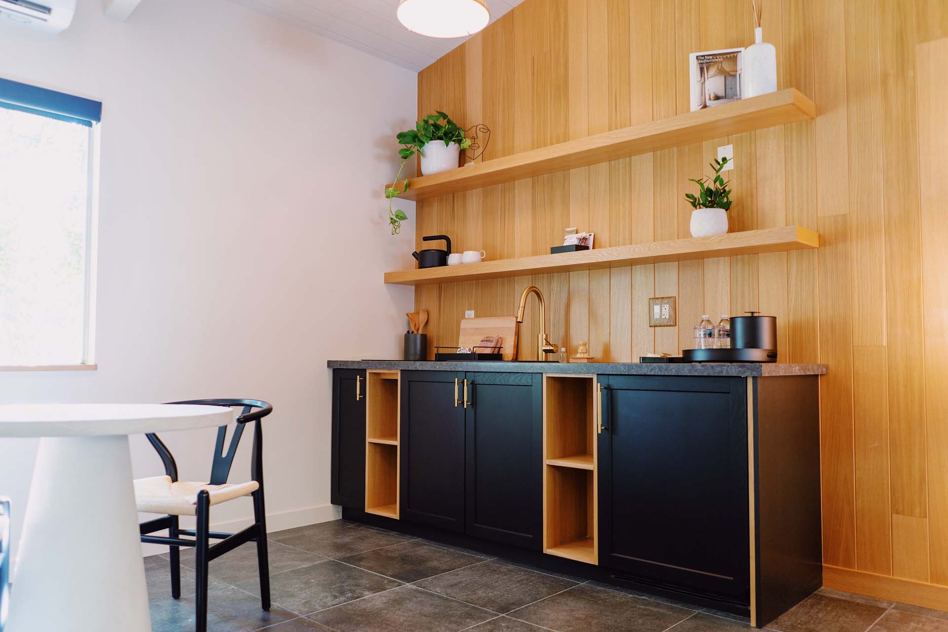 A kitchenette with black cabinets, wooden shelves, and a sink
