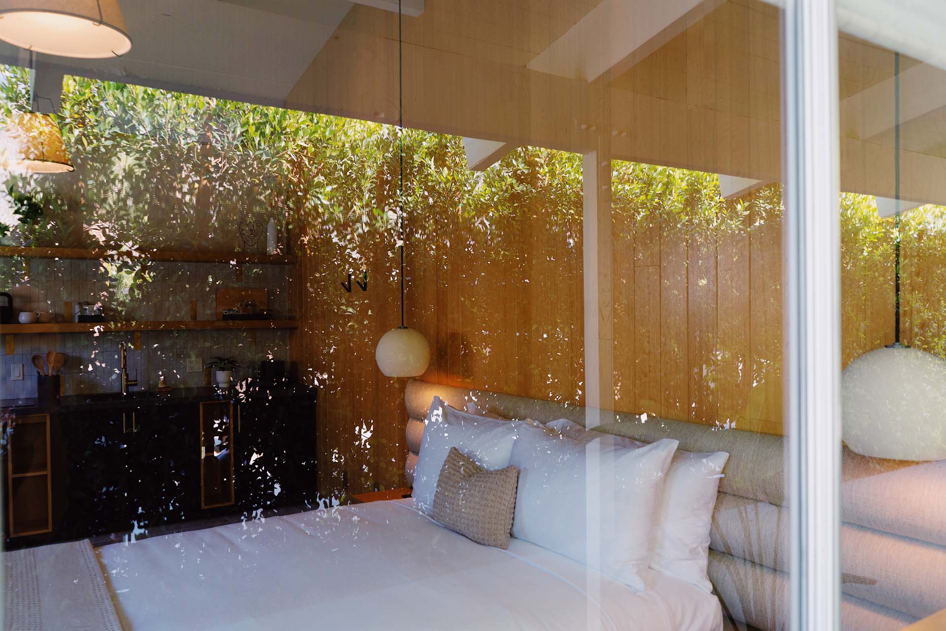 A room with a bed, kitchenette, and window with rain shower, surrounded by wooden walls.