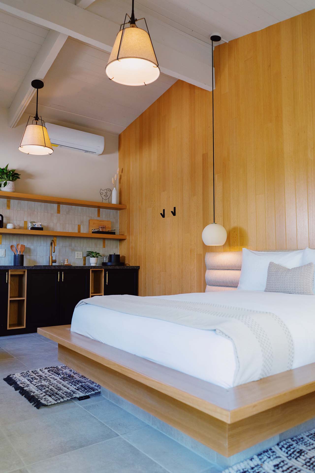 A modern hotel room with a platform bed, kitchenette, and pendant lights