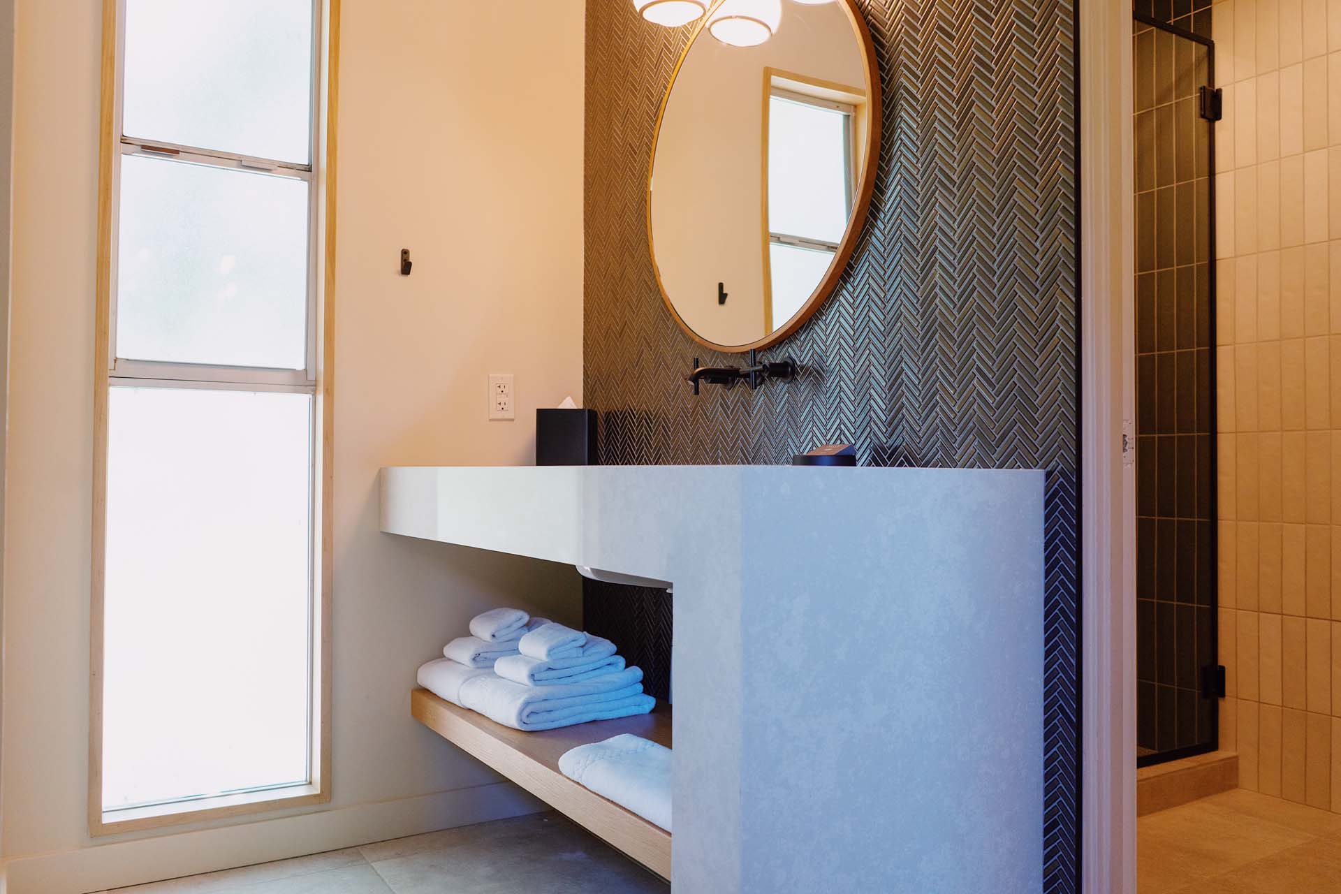 A modern bathroom sink area with a floating sink, round mirror, and tiled wall