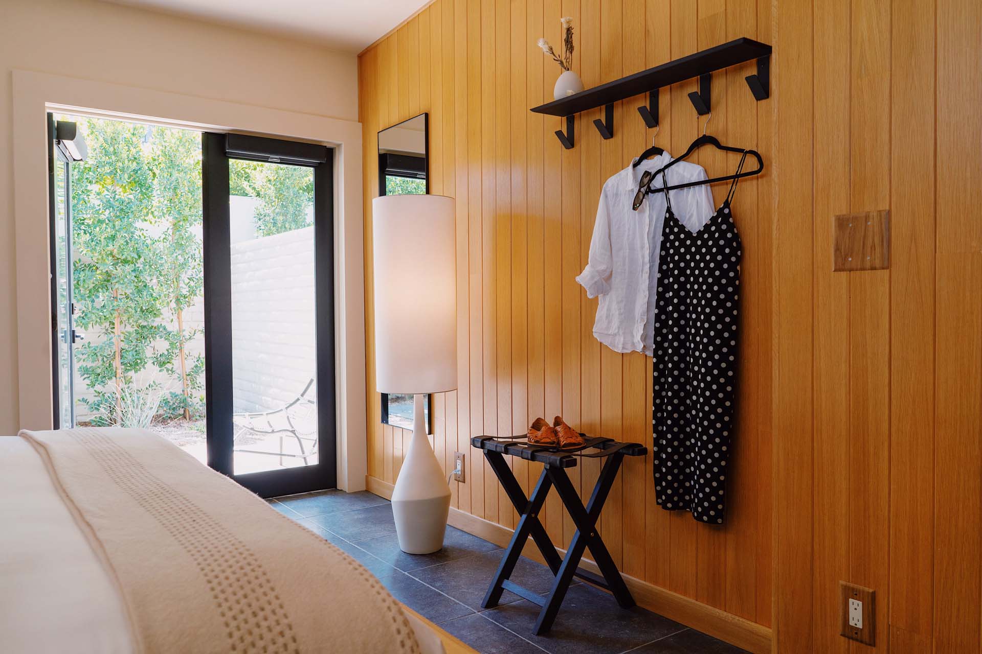 A hotel room with wood paneling, a lamp, and a luggage rack with clothes hanging on the wall.