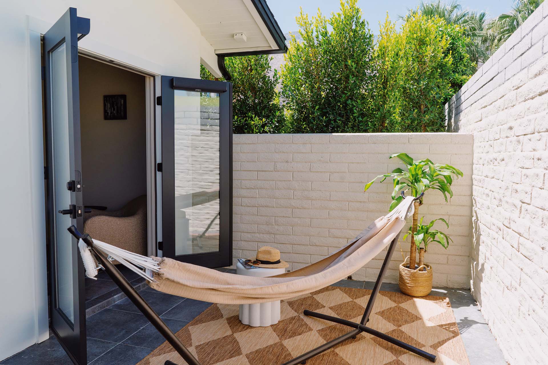 A hammock and a plant on a small outdoor patio with a door leading inside.