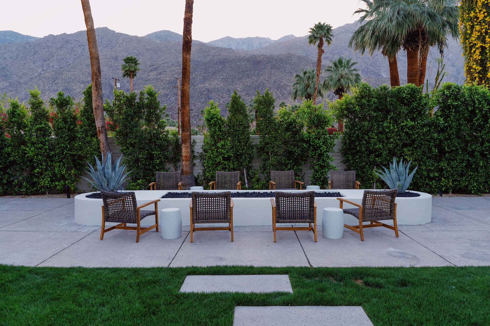 A seating area with a fire pit and chairs in front of a hedge with a mountain view.