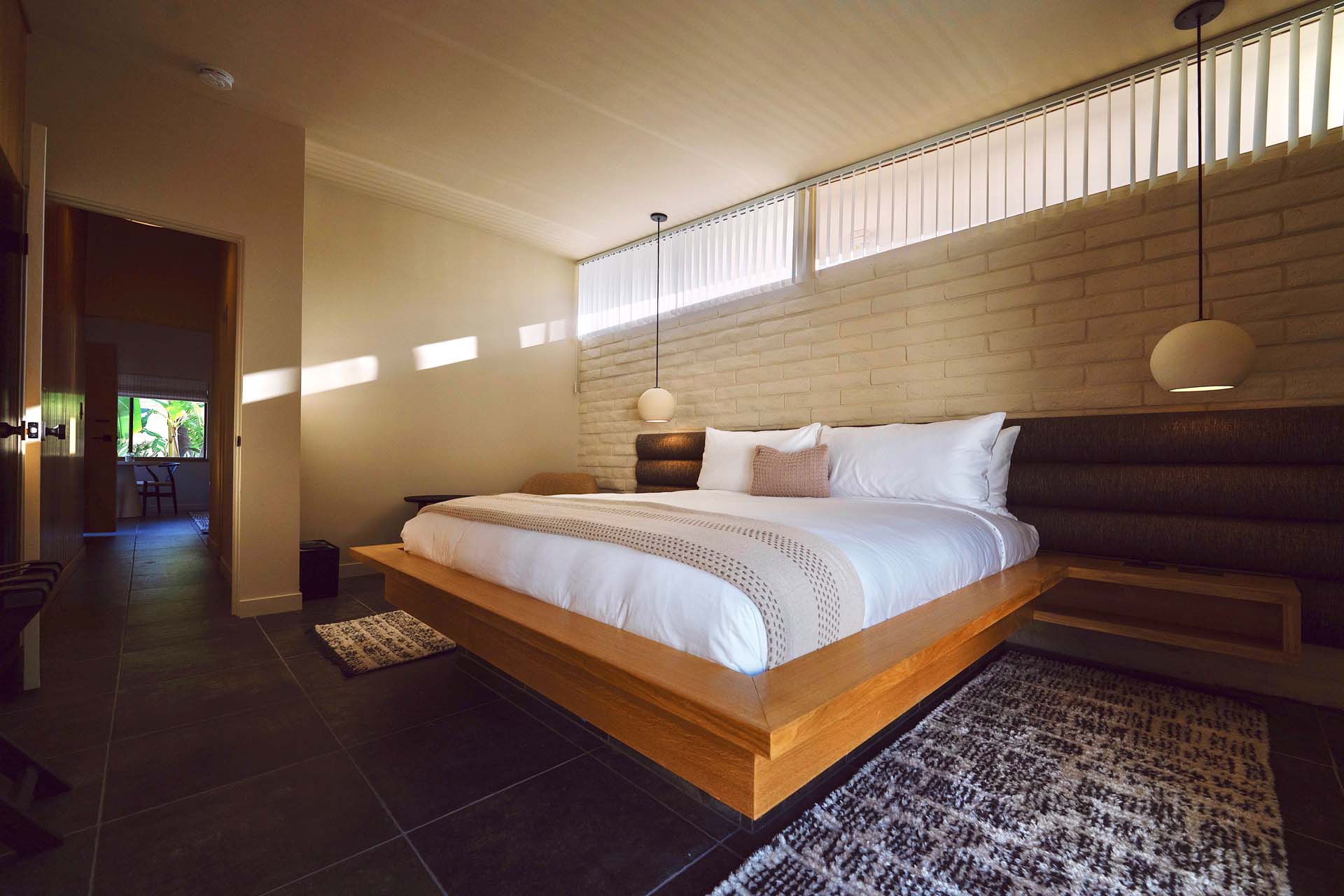 A modern hotel room with a large bed, wooden accents, and a brick wall.