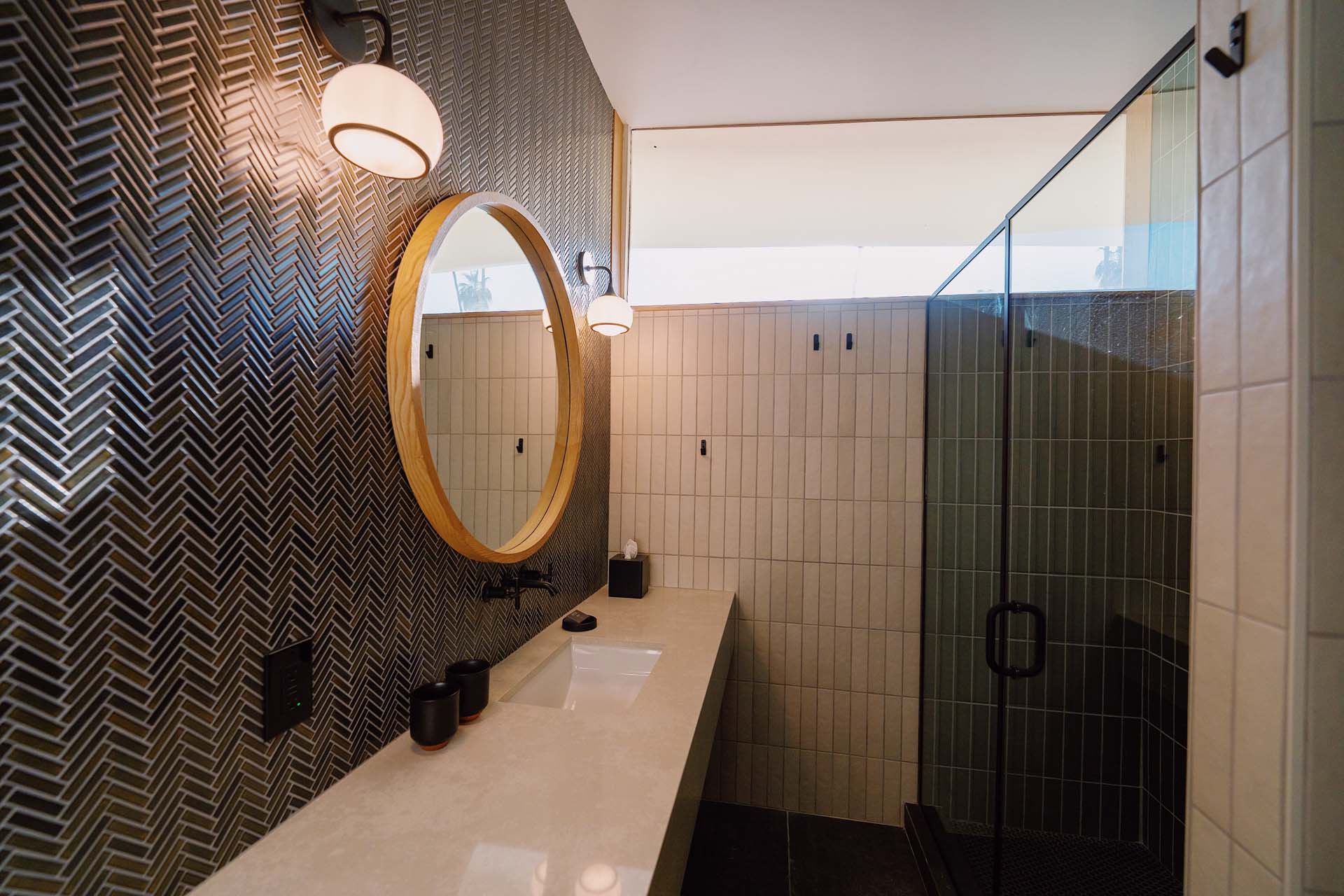 A modern bathroom with a glass-enclosed shower, marble countertop, and herringbone tile wall.